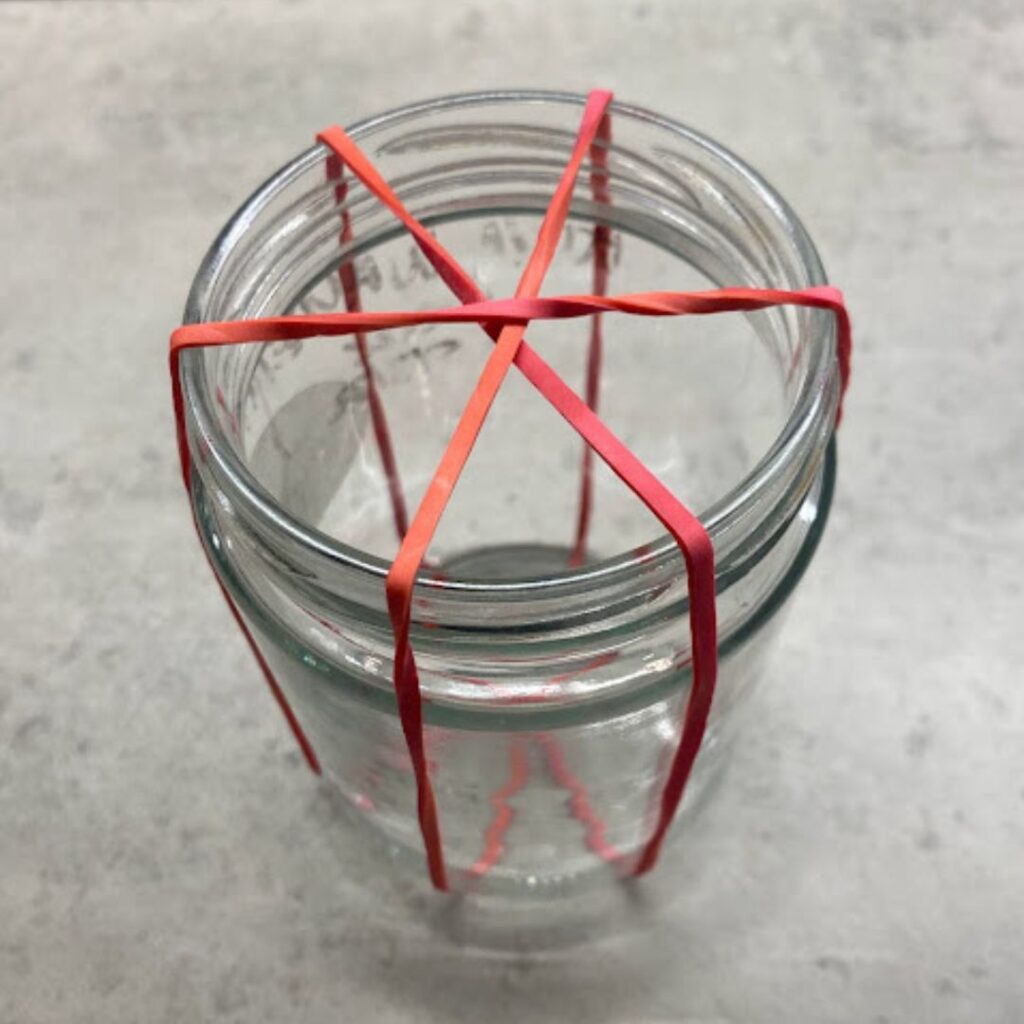 covering  a jam jar in rubber bands to help stop the cuttings from falling into the water